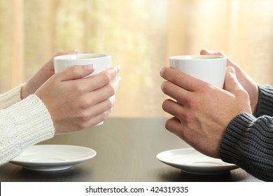 Profile of hands of a couple holding coffee cups over a table in winter in an apartment with a window in the background - Powered by Shutterstock