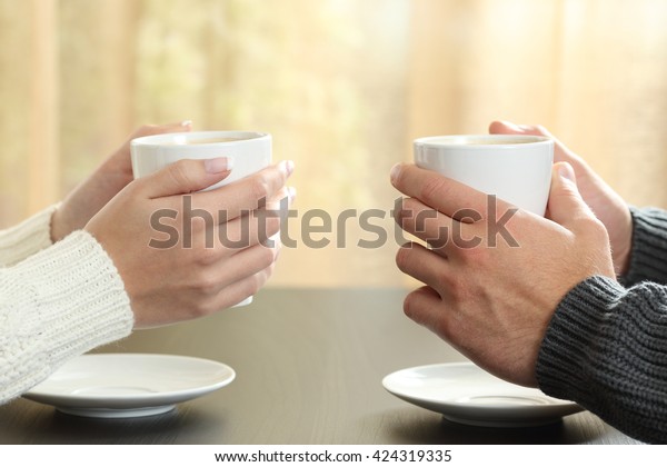 冬の間 テーブルの上にコーヒーカップを持つカップルの手の形と 背景に窓のあるアパート の写真素材 今すぐ編集