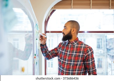 Profile of handsome african man with beard standing and writing on whiteboard