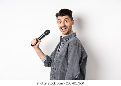 Profile Of Handsome Smiling Man Holding Mic, Turn Head At Camera With Excited Face, Singing Karaoke And Perform Standup, Standing On White Background