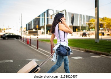 Profile Of Happy Caucasian Woman Pulling Rolling Suitcase And Carrying Handbag While Talking On Mobile Phone Outdoors In City