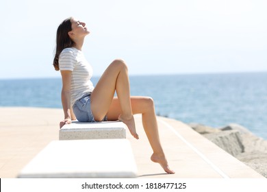Profile of a happy woman with long waxed legs breathing fresh air sitting on a bench on the beach
