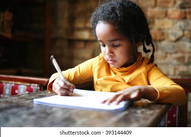 Profile of little African girl writing  at home.
