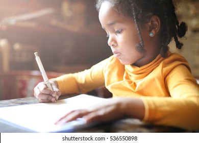 Profile of little African girl writing  at home.
