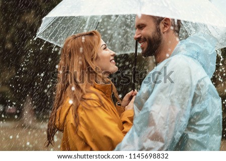 Profile of loving couple spending date outside. They are standing under umbrella and looking at each other with care and smile