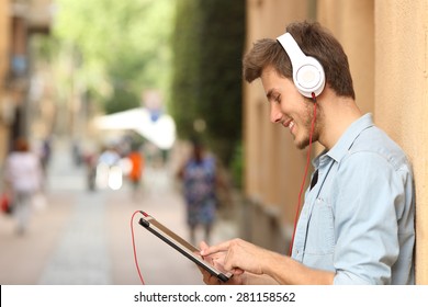 Profile Of A Man Using A Tablet With Headphones On The Street And Touching The Screen With The Finger