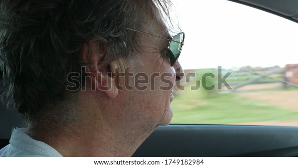 \
Profile of older man face driving on road with\
landscape passing by