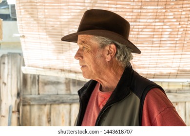 Profile Ortrait Of Handsome Baby Boomer Senior Man Posing Outdoors Underneath A Shade Cloth, Wearing A Fedora Hat