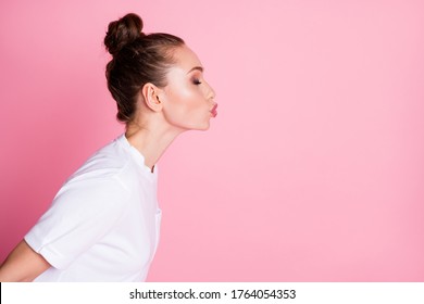 Profile photo of attractive lady funny bun hairdo sending air kisses side empty space coquettish lovely girlish person eyes closed wear white t-shirt isolated pastel pink color background