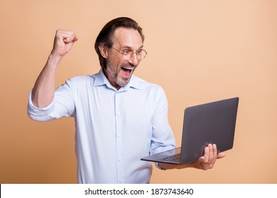 Profile photo of excited man hold netbook raise fist open mouth wear eye wear shirt isolated beige color background - Shutterstock ID 1873743640
