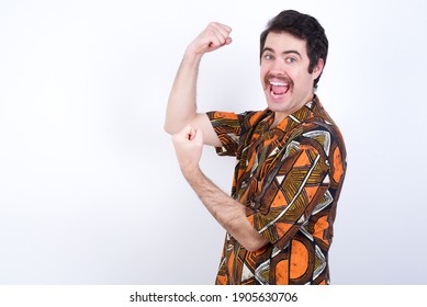 Profile Photo Of Excited Young Caucasian Man Wearing Generic Pattern Printed Shirt Against White Wall Raising Fists Celebrating Black Friday Shopping