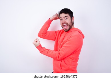Profile photo excited young Caucasian bearded man wearing pink hoodie against white background raising fists celebrating black Friday shopping