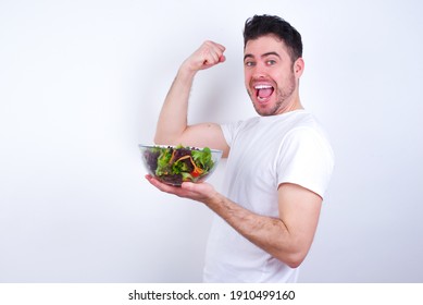 Profile photo of excited Young handsome Caucasian man holding a salad bowl against white background raising fists celebrating black Friday shopping