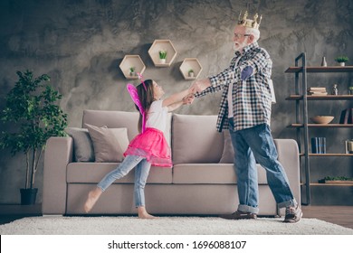 Profile photo of funny aged old grandpa little pretty granddaughter acting fairy stage costumes good mood hold arms dancing stay home quarantine safety modern interior living room indoors