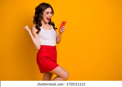 Profile photo of funny youngster lady open mouth hold telephone read blog comment raise fist win giveaway present wear casual white tank-top red skirt isolated yellow color background