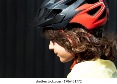 Profile Photo Of A Little Boy With Long Hair Wearing A Safety Helmet Riding A Bike. Black Background. Copy Space