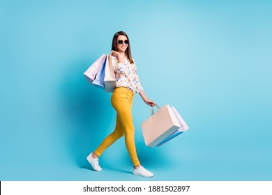 Profile photo of lovely young girl walk carry store bags wear sunglass geometry print shirt yellow trousers isolated blue color background