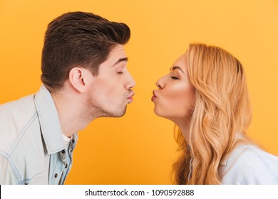 Profile photo of young beautiful people in love expressing love and affection while kissing each other with closed eyes isolated over yellow background