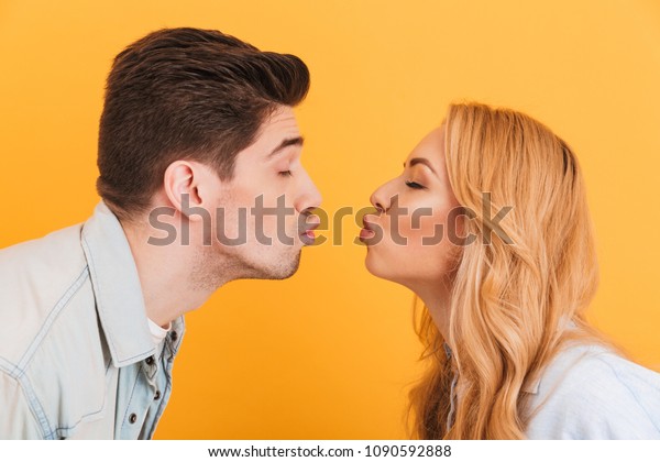 Profile photo of young beautiful people\
in love expressing love and affection while kissing each other with\
closed eyes isolated over yellow\
background