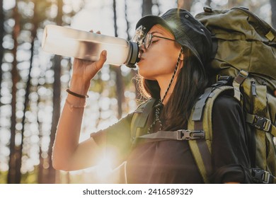 Profile photo of young woman drinking water in forest, sun flare. Female explorer traveler adventurer rehydrating with cold drink, relaxing feeling thirsty in solo trip - Powered by Shutterstock