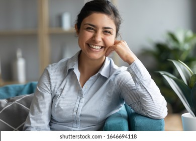 Profile picture of smiling beautiful millennial Indian girl sit rest on couch in living room, portrait of happy young ethnic woman relax on comfortable sofa at home look at camera feel positive