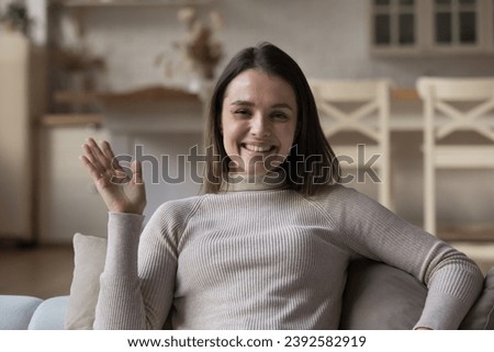 Profile picture of young pretty woman sits on couch make video conferencing call at home, smile look at camera feel happy enjoy distancing talk to family living abroad. Virtual meeting event concept