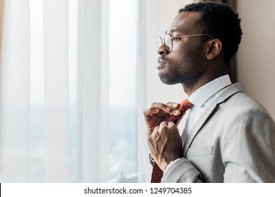 profile portrait of african american businessman adjusting red tie and looking at window - Powered by Shutterstock