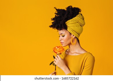 Profile portrait of a beautiful young woman smelling yellow orange rose and looking down, isolated on yellow background