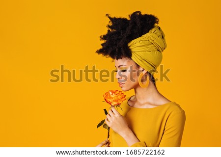 Profile portrait of a beautiful young woman smelling yellow orange rose and looking down, isolated on yellow background