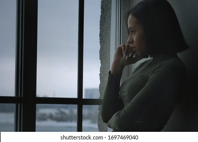 Profile portrait of fashionable beautiful african american young woman with short straight hair standing near the window in the dark and looking away, depressed thoughtful young american african woman