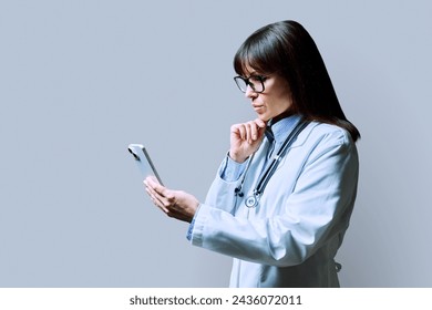 Profile portrait of female doctor using smartphone on gray background - Powered by Shutterstock