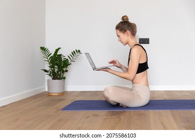 Profile Portrait Of Girl Is Sitting In Turkish Pose, Crossing Her Legs With Straight Back, Holding A Laptop, Searching Or Texting, Dressed In Sport Outfit, Bun Of Fair Hair, At Home,green Plant In Pot