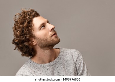 Profile portrait of gorgeous cute handsome young man with perfect features, bristle and reddish hair posing at blank copyspace wall in jumper, looking up with inspired dreamy facial expression