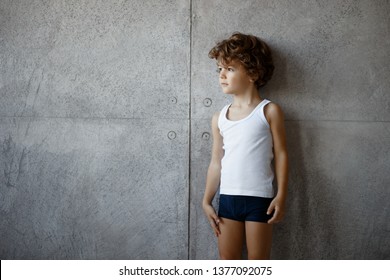 Profile portrait of a handsome little boy in underwear posing on concrete wall, looking a one side, copy space.