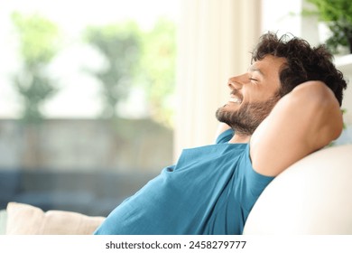 Profile portrait of a happy handsome man resting and relaxing sitting on a couch at home - Powered by Shutterstock