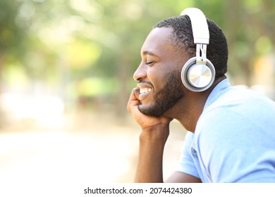 Profile Portrait Of A Happy Man With Black Skin Listening To Music With Headphones In A Park