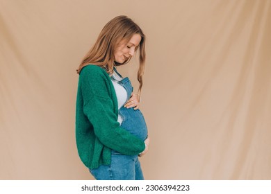 profile portrait of happy pregnant woman touching her belly satisfied - blond caucasian woman in dungarees