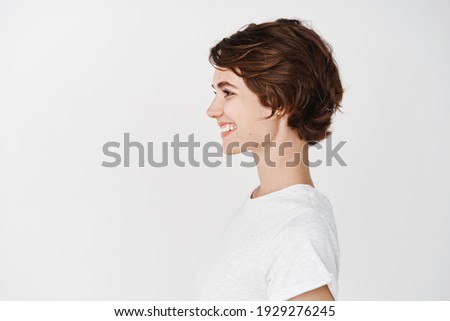 Profile portrait of healthy natural woman with short hairstyle, smiling and looking left at empty space, standing in t-shirt on white background.
