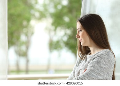 Profile Portrait Of A Longing Woman Looking Outdoors Through A Window At Home Or Hotel Room With A Green Background