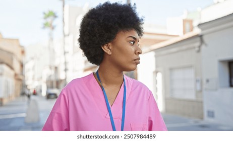 Profile portrait of a pensive african american woman in pink scrubs with a lanyard standing outdoors. - Powered by Shutterstock