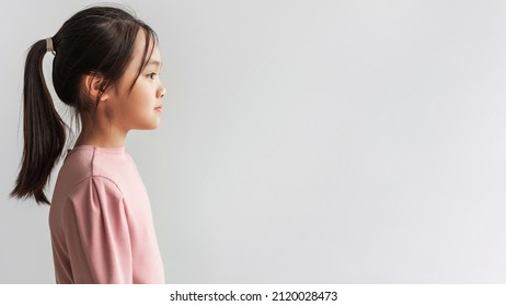 Profile Portrait Of Serious Asian Preteen Girl Looking Aside At Copy Space Standing On Gray Background, Wearing Pink Longsleeve. Kids Fashion And Beauty. Panorama, Studio Shot