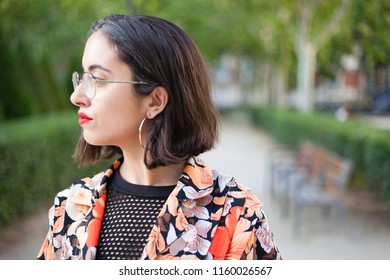 Profile Portrait Shot Of Trendy Actual Woman Serious And Confident On A Madrid Outdoors Park City Background Wih Make Up, Big Ear Rings, Flower Shirt And Fishnet. Spanish Empowered Woman.