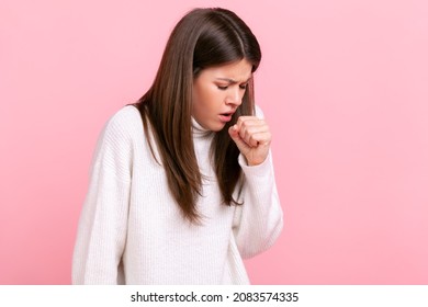 Profile Portrait Of Young Adult Brunette Sick Woman Coughing, Catches Cold, Having High Temperature, Wearing White Casual Style Sweater. Indoor Studio Shot Isolated On Pink Background.