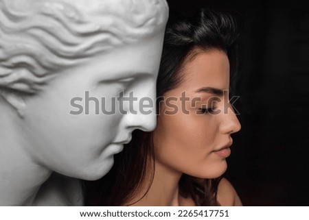 Profile portrait of a young beautiful woman standing next to a gypsum sculpture of Venus