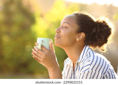 Profile of a relaxed black woman drinking coffee and smelling aroma in a park - Powered by Shutterstock