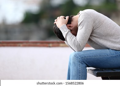 Profile of a sad man complaining sitting on a bench alone in a town - Shutterstock ID 1568522806