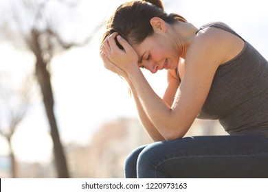 Profile Of A Sad Teen Crying Desperately Sitting On A Bench In A Park