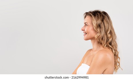 Profile Shot Of Beautiful Smiling Middle Aged Woman Standing Wrapped In Towel Over Light Gray Background, Attractive Mature Female Looking At Copy Space, Enjoying Beauty Care, Panorama