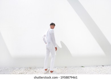 profile shot of a Fashion style photo of a full body back handsome man
 in white shirt and white pants , posing on white building


