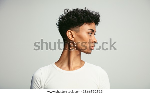 Profile shot of a gender fluid\
man wearing earring. Young androgynous man against white\
background.